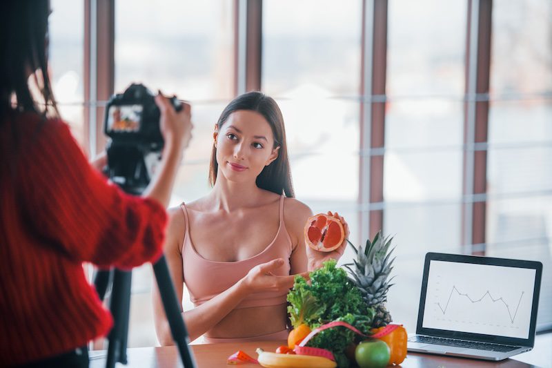 Fitness model have photoshoot by female photographer indoors by the table with healthy food